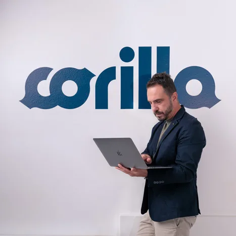 Francesco al PC in piedi davanti alla parete con logo Corilla